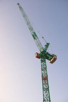 Top portion a tall tower crane at sunrise with a bright sky background. Modern construction machinery with fresh green and orange colors. metal frame.