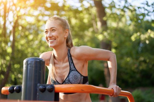 Sportive female training dip exercise machine outdoor gym summer park Middle age caucasian woman dressed sportswear workout outside on simulator sport ground. Healthy lifestyle concept