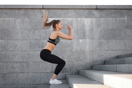 Urban sporty woman training. Female athlete doing squat jumps on urban stairs. Fitness motivation Healthy lifestyle concept