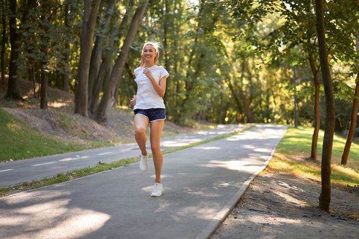 Woman running asphalt road summer park Active sporty caucasian female morning workout Healthy lifestyle concept. Athletic person sportswear exercises Dressed white t-shirt full length