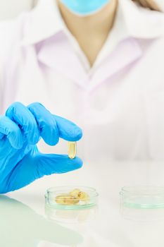 Close up Scientist hands putting in nitrile blue latex gloves holding Omega 3 capsule in labcoat wearing nitrile gloves, doing experiments in lab