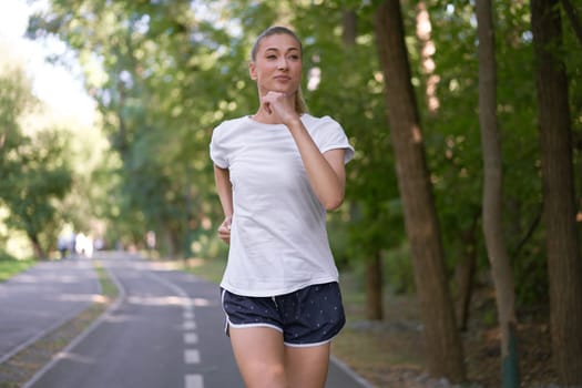 Woman running asphalt road summer park Active sporty caucasian female morning workout Healthy lifestyle concept. Athletic person sportswear exercises Dressed white t-shirt