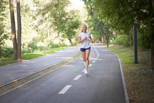 Woman running asphalt road summer park Active sporty caucasian female morning workout Healthy lifestyle concept. Athletic person sportswear exercises Dressed white t-shirt full length