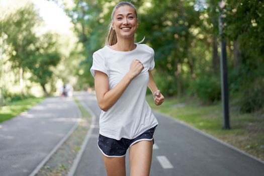 Woman running asphalt road summer park Active sporty caucasian female morning workout Healthy lifestyle concept. Athletic person sportswear exercises Dressed white t-shirt