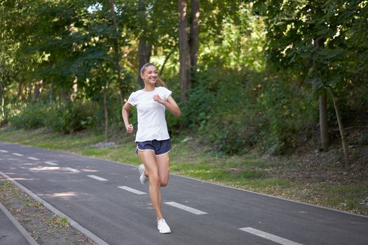 Woman running asphalt road summer park Active sporty caucasian female morning workout Healthy lifestyle concept. Athletic person sportswear exercises Dressed white t-shirt full length