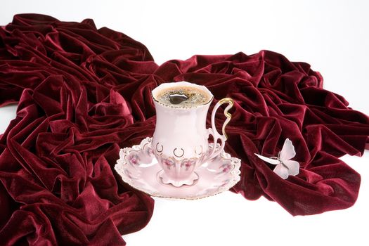 Cup of tea, dark- red velvet and butterfly on a studio background