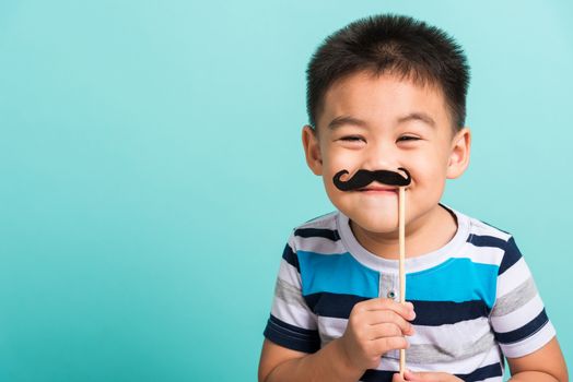 Funny happy hipster kid holding black mustache props for the photo booth close face, studio shot isolated on a blue background, Men health awareness, Prostate Cancer Awareness