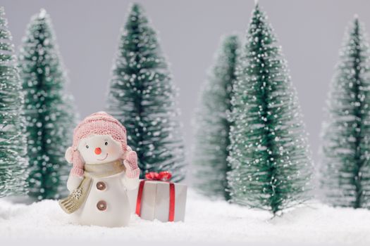 Small cute toy snowman with gift in forest in snow Christmas card design