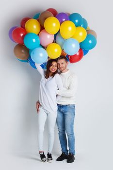 Young couple with many colorful balloons on white background