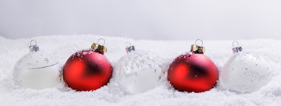 Christmas border of red and white baubles ornaments in snow on light background