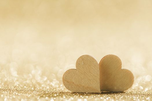 Two small handmade wooden hearts on bright golden lights bokeh background Valentines day card