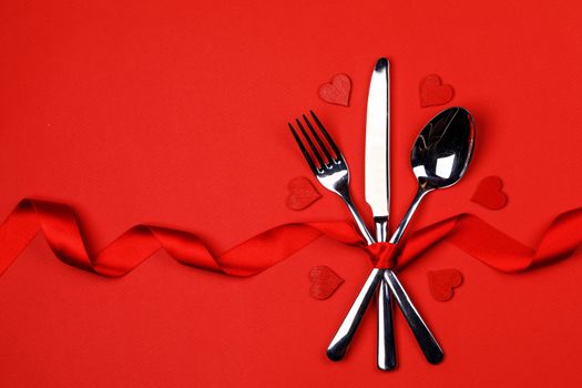Cutlery set tied with silk ribbon and hearts on red background Valentine day dinner concept
