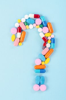 A question mark from laid out of medicine pills on blue background.