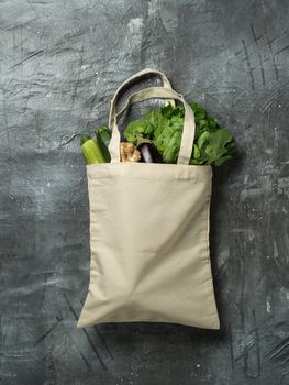 Cotton tote bag with vegetables on gray background. Organic cotton canvas bag with fresh zucchini, eggplant, ginger root, broccoli and salad. Vertical. Mock up for design or your logo