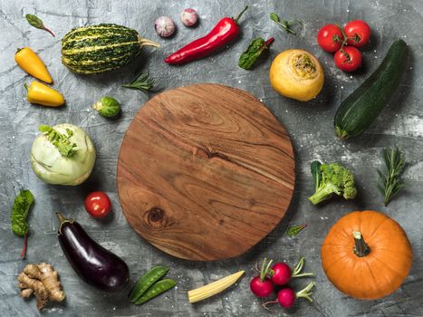 Selection of vegetables with round wooden tray in center with copy space for text or design. Zucchini, pumpkin, tomatoes, cabbages, peppers, radish and herbs top view or flat lay