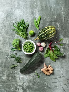 Green vegetables and herbs on gray background, top view.Still life with green peas, zucchini, bean-pod, pumpkin, ginger, garlic, broccoli, tarragon, brussels sprouts, rosemary, microgreens and mangold