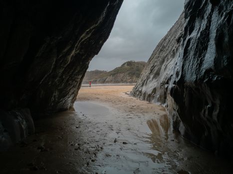 A small cave looking out to the sand Caswell Bay Beach in Gower, Wales, UK on a cloudy and wet day.