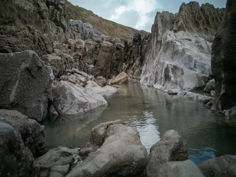 A large rock pool sitting between the tides with smooth rocks from sea erosion. Location: Caswell Bay, Gower, Wales, UK