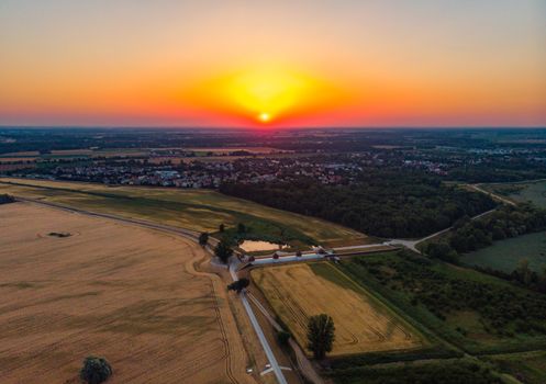 Aerial view to rising sun over fields village and forest at morning