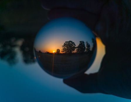 Morning rising sun catched in crystal glassy lensball with trees silhouettes