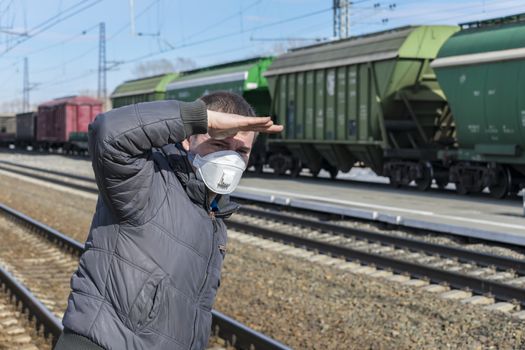 Man at the railway station waiting for his train, covering his face with his hand from the sun