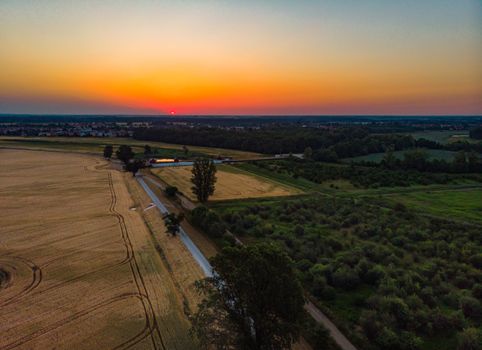 Aerial view to rising sun over fields village and forest at morning