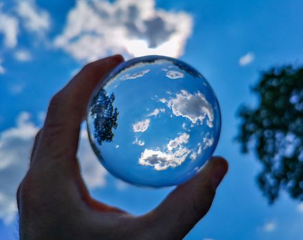Upward view to cloudy sky and tree crown by the crystal glassy lensball