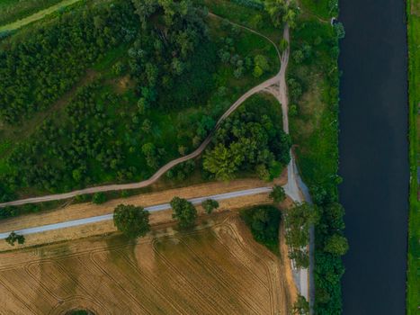 Aerial top down look to streets and paths between forest and fields and river on side