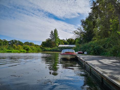 Old boat near wooden platform on river between bushes and trees