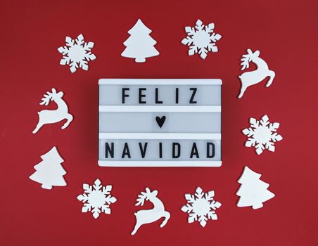 Light box with Feliz Navidad phrase, Spanish Merry Christmas on red background with wooden toys.