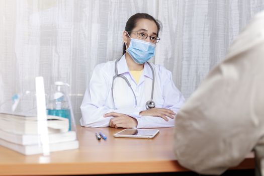 Doctor wear protective face mask working in her clinic and listening to the patient, Doctor looking and listening explaining his symptoms. healtcare and assistance concept