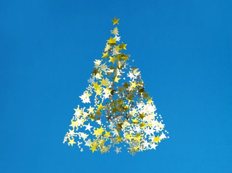 Christmas tree shape from golden confetti stars on blue paper.