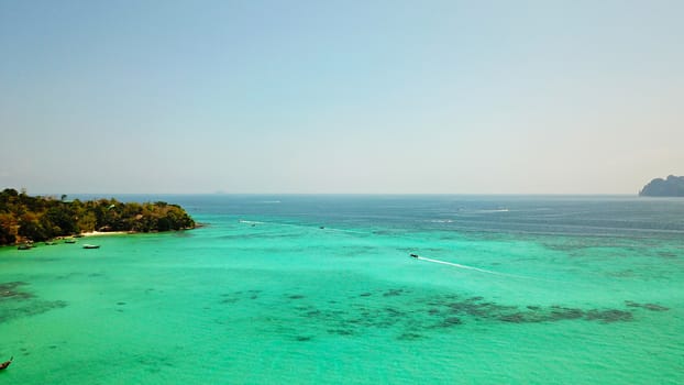 Turquoise clear water. Yachts, boats floating. Water Gradient from light to dark blue. Phi Phi don island, shooting from a drone from the air. White sand, green trees, palm trees and large hills.