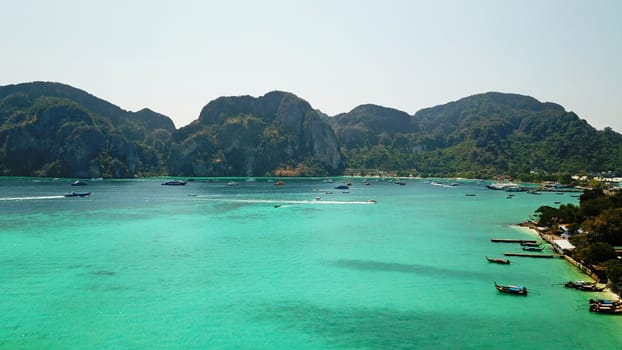 Turquoise clear water. Yachts, boats floating. Water Gradient from light to dark blue. Phi Phi don island, shooting from a drone from the air. White sand, green trees, palm trees and large hills.