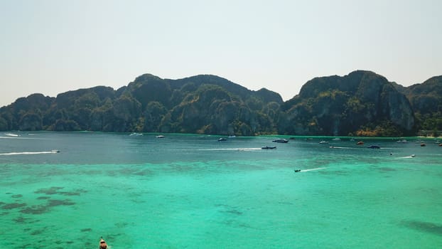 Turquoise clear water. Yachts, boats floating. Water Gradient from light to dark blue. Phi Phi don island, shooting from a drone from the air. White sand, green trees, palm trees and large hills.