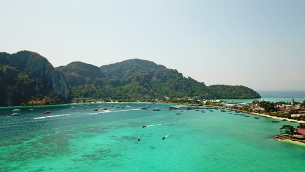 Turquoise clear water. Yachts, boats floating. Water Gradient from light to dark blue. Phi Phi don island, shooting from a drone from the air. White sand, green trees, palm trees and large hills.