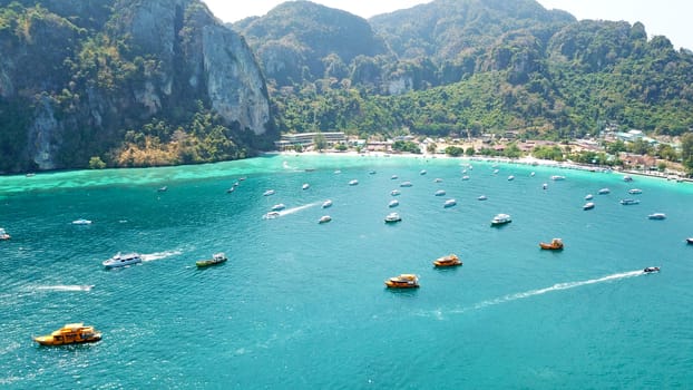 Turquoise clear water. Yachts, boats floating. Water Gradient from light to dark blue. Phi Phi don island, shooting from a drone from the air. White sand, green trees, palm trees and large hills.