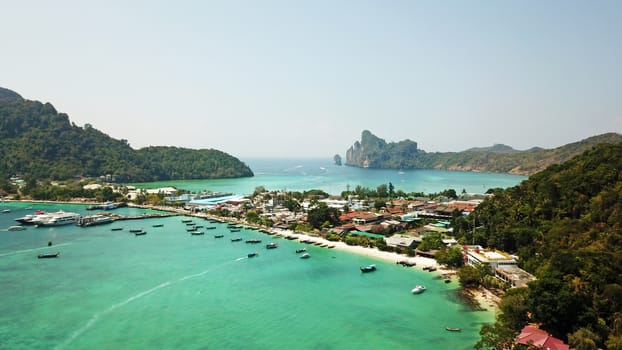 Turquoise clear water. Yachts, boats floating. Water Gradient from light to dark blue. Phi Phi don island, shooting from a drone from the air. White sand, green trees, palm trees and large hills.