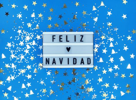 Light box with Feliz Navidad phrase, Spanish Merry Christmas on blue background with confetti.