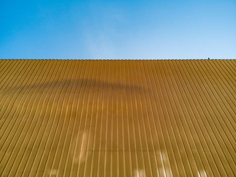 Curvy yellow metal wall of building with pigeon on top