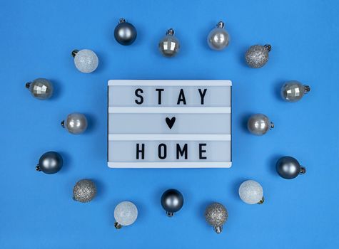 Light box with stay home quote on blue background with Christmas balls.