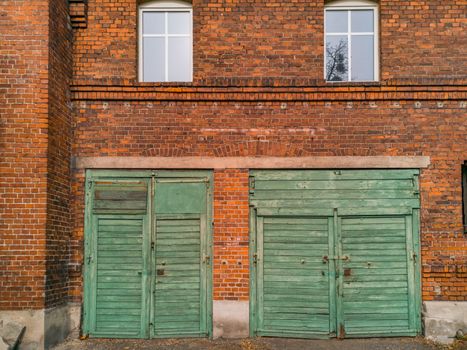 Two green wooden gates to garages in red brick building