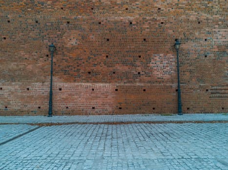 Red brick wall with two high black lamps near pavement