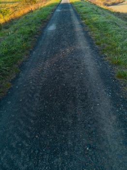 Long path full of small stones between green and yellow fields and bushes