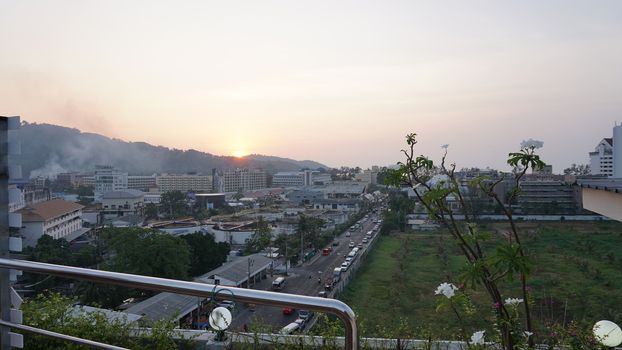 Drone view of the city of Patong, Phuket island. Houses of different heights stand on the beach. Green hills of the island. On the roof of houses pools, people swim. On the road go scooters and cars.