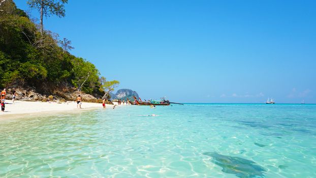 The beach of bamboo island. People relax, swim. White sand, clear blue water, bright sky. Thai boat near the shore. The beach is similar to the Maldives. Tropical island in the ocean. Thailand.