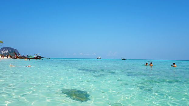 The beach of bamboo island. People relax, swim. White sand, clear blue water, bright sky. Thai boat near the shore. The beach is similar to the Maldives. Tropical island in the ocean. Thailand.