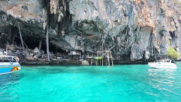 A large cave with hanging stalactites. Viking cave in Thailand. Turquoise clear water. Large blocks of gray stones. A small Bush grows. The entrance from the ocean. Unusual place.