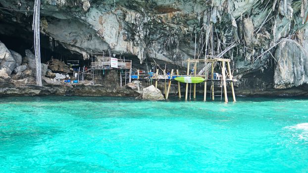 A large cave with hanging stalactites. Viking cave in Thailand. Turquoise clear water. Large blocks of gray stones. A small Bush grows. The entrance from the ocean. Unusual place.