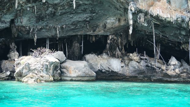A large cave with hanging stalactites. Viking cave in Thailand. Turquoise clear water. Large blocks of gray stones. A small Bush grows. The entrance from the ocean. Unusual place.
